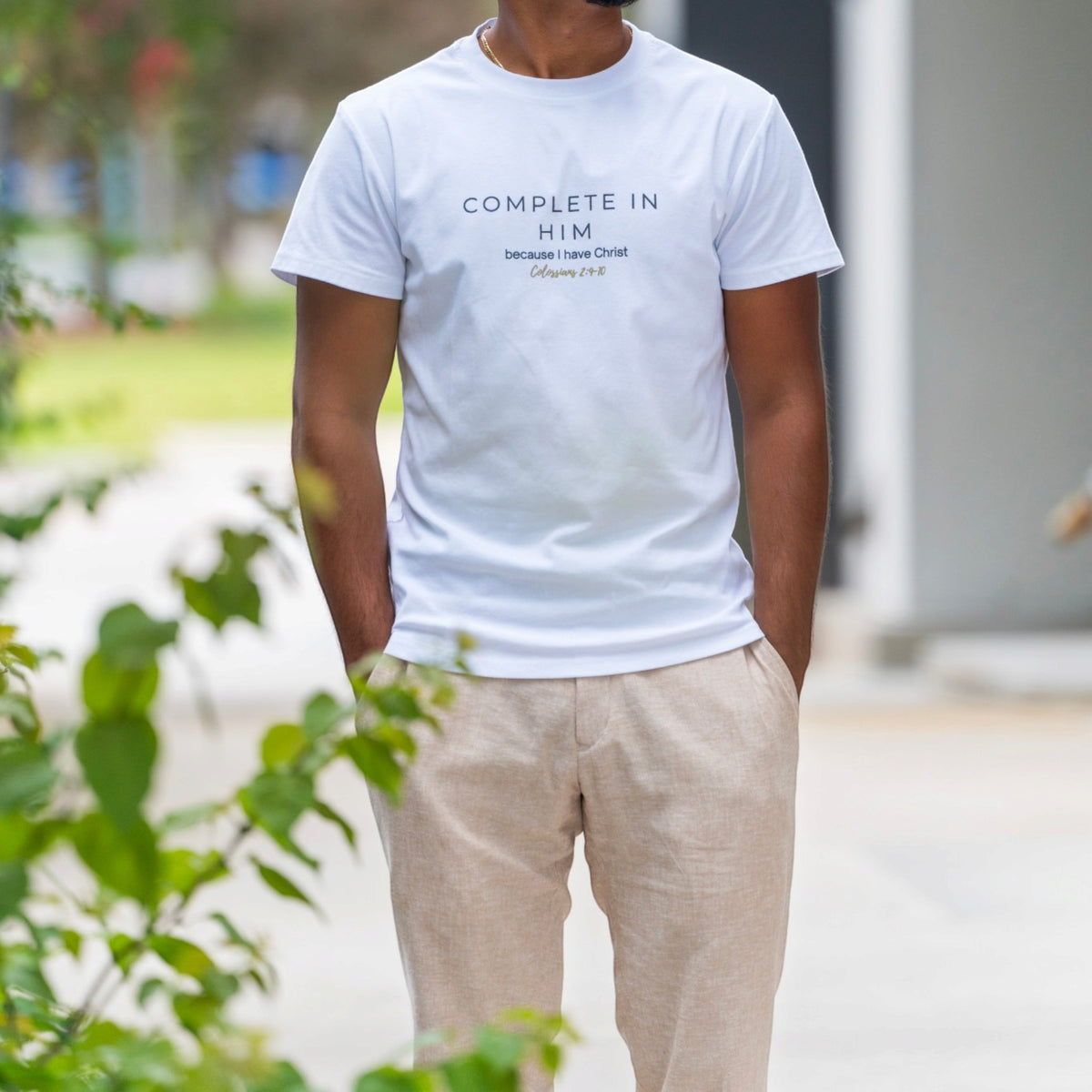 Men's white Complete In Him shirt by ADM Driven featuring a Colossians 2:10 message, styled with beige trousers.