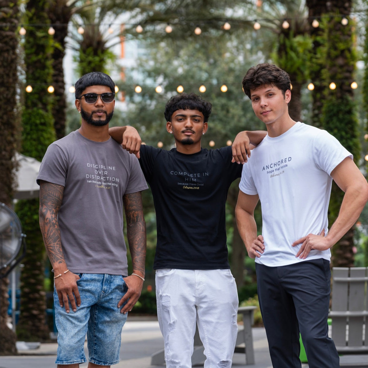 Three men modeling ADM Driven shirts featuring Discipline Over Distraction in gray, Complete In Him in black, and Anchored in white.