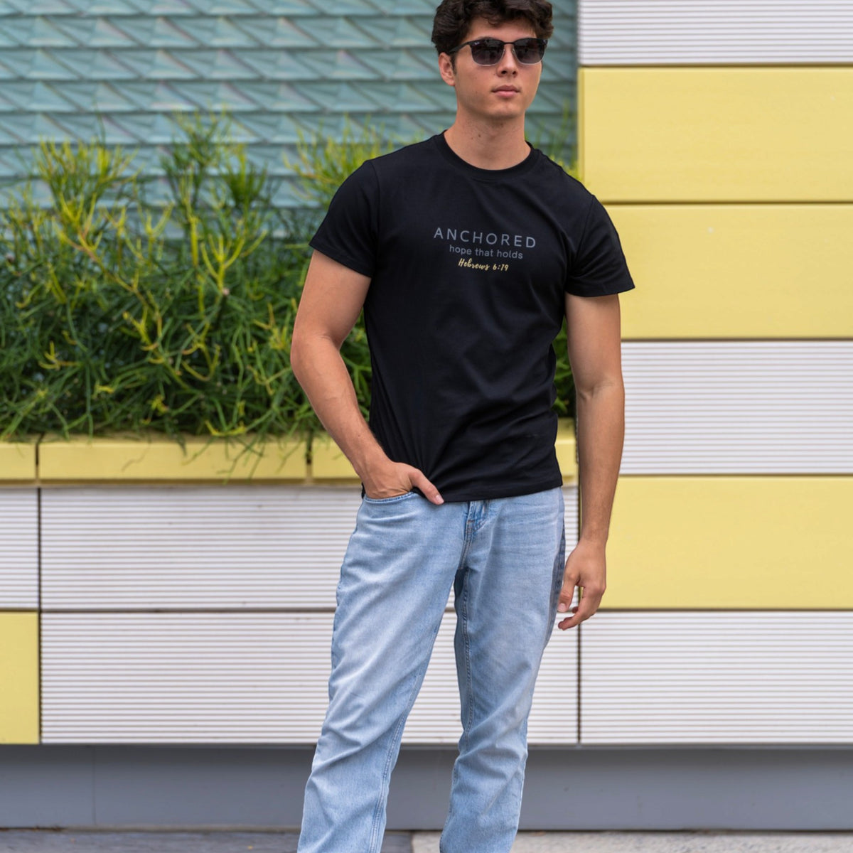 Man wearing the black Anchored men's shirt by ADM Driven, featuring a message inspired by Hebrews 6:19, styled with blue jeans.