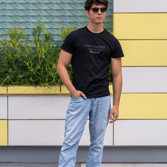 Man wearing the black Anchored men's shirt by ADM Driven, featuring a message inspired by Hebrews 6:19, styled with blue jeans.
