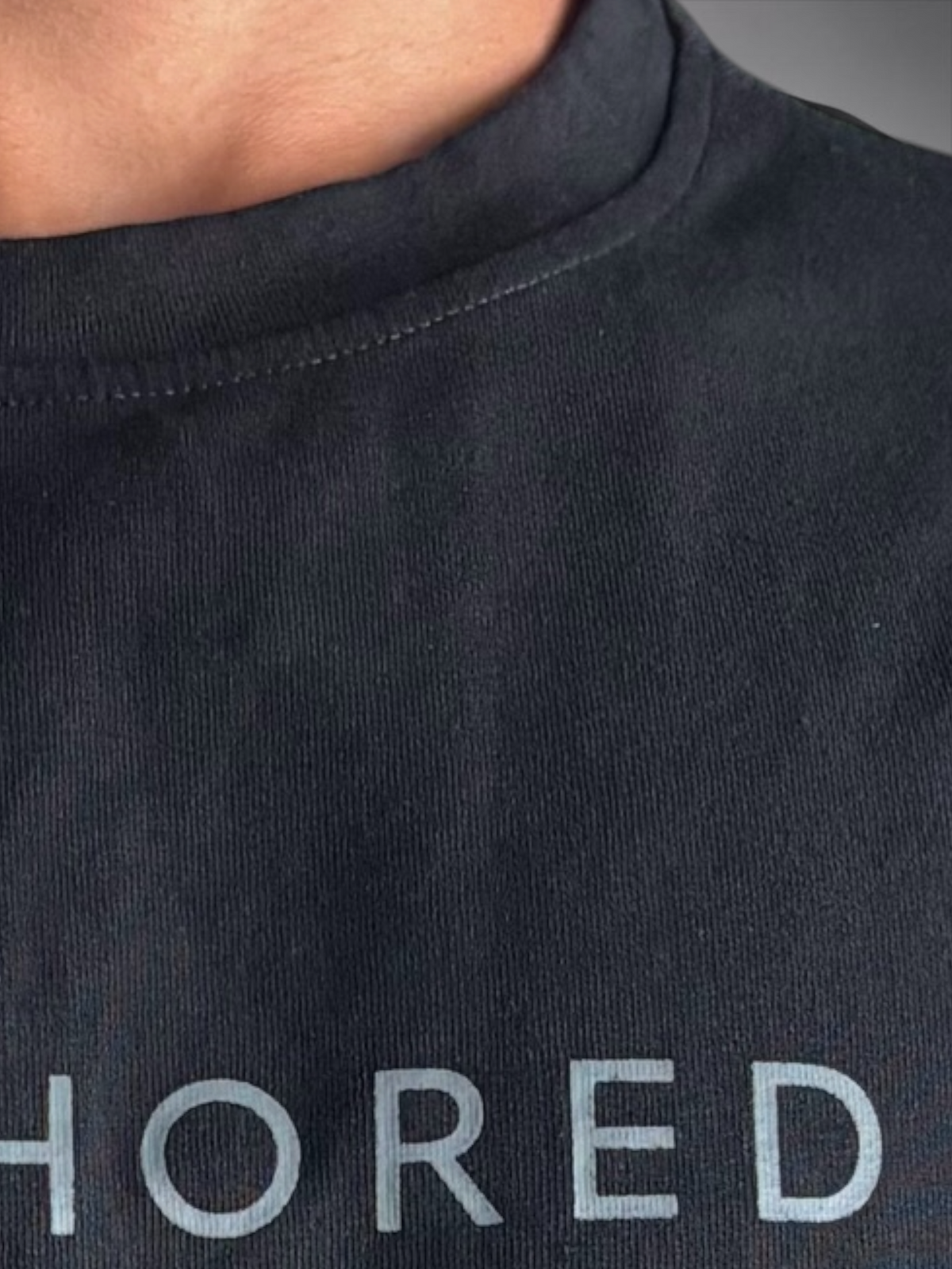 Close-up of the black ANCHORED T-shirt showing crew-neck stitching, fabric texture, and part of the chest print.