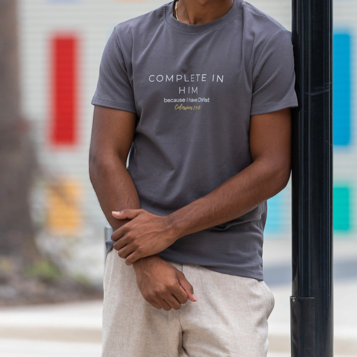 Men's charcoal grey Complete In Him shirt by ADM Driven featuring a Colossians 2:10 message, styled with beige trousers.