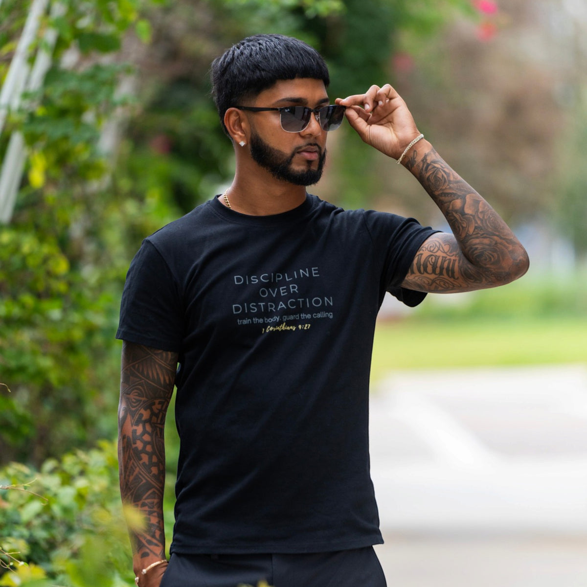 Man wearing the black Discipline Over Distraction men's shirt by ADM Driven, featuring a message inspired by 1 Corinthians 9:27, outdoors.